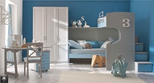 Arredamenti camerette stile tradizionale e sobrio colore azzurro. Letto a casgtello, scalini cassetti colore blu vicino parete colore blu. Armadio colore bianco e scrivania beige. Bambole giocattoli animali in giro per la stanza