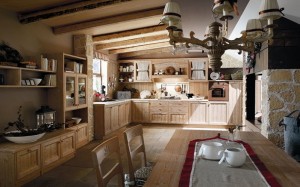 Kitchen country furnishings. Callesella rustic kitchen, classic and cozy style. Wood color like hay, with table near fireplace. Ancient chandelier above table.